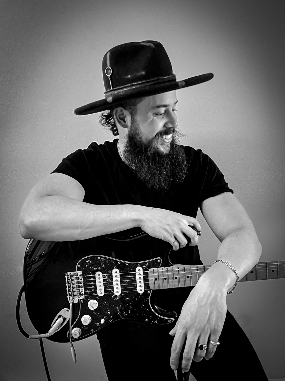 Will Plus smiling with his electric guitar in a candid black-and-white portrait